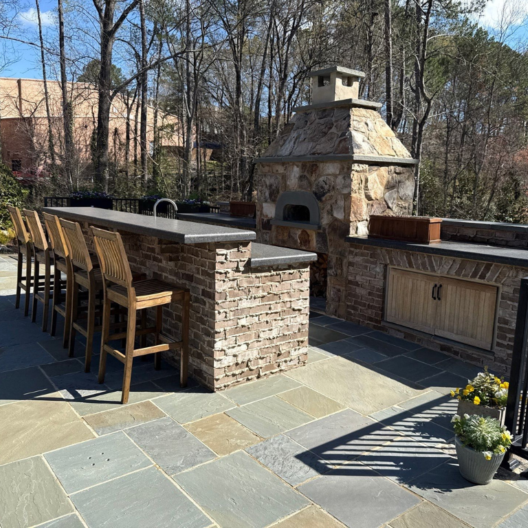 Custom outdoor kitchen and stone fireplace with bar seating and bluestone patio by Legacy Stonescapes