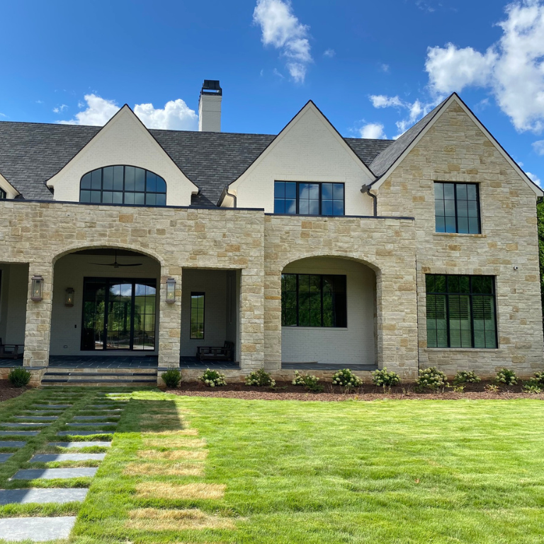 Rear exterior of custom home with limestone facade, covered patio, and stepping stone walkway