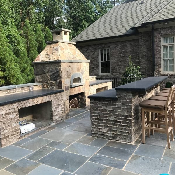 Custom outdoor kitchen and stone fireplace with bar seating and bluestone patio by Legacy Stonescapes